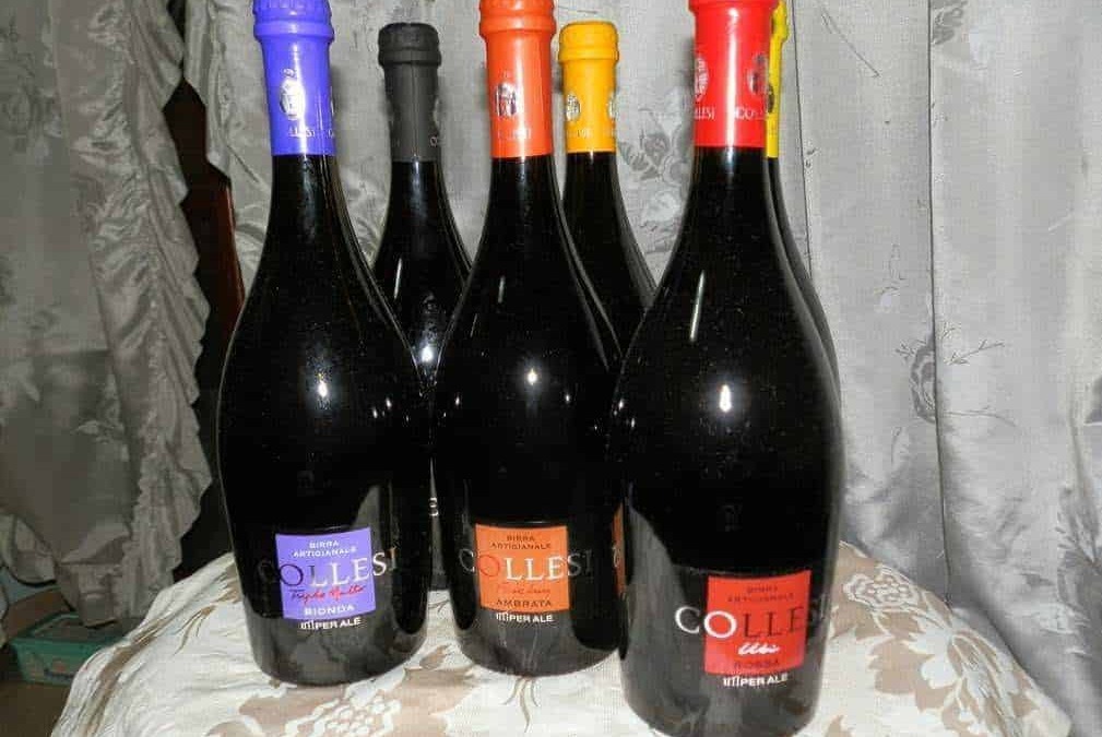 Bottiglie di vino rosso con etichette colorate, posizionate su un tavolo con tende di velluto sullo sfondo, rappresentano vini artigianali italiani di alta qualità.