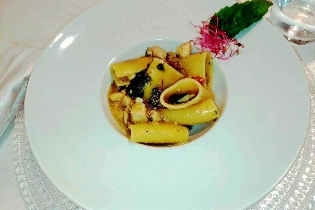 Farfalle con seppie e salsa al nero di seppia decorata con erbe fresche e fiori commestibili, presentata su piatto elegante in ristorante di alta cucina.