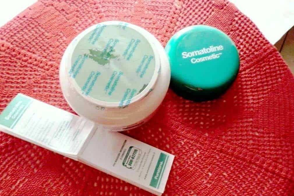 Prodotti cosmetici Somatoline Cosmetica su un tavolo rotondo di tessuto rosso naturale, tra cui crema viso e crema anti cellulite per cura e bellezza della pelle.