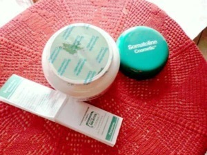 Prodotti cosmetici Somatoline Cosmetica su un tavolo rotondo di tessuto rosso naturale, tra cui crema viso e crema anti cellulite per cura e bellezza della pelle.
