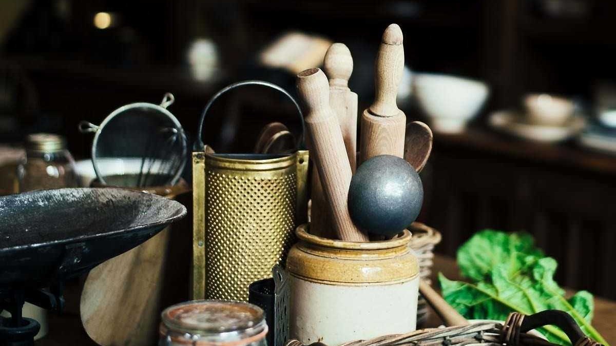 Set di utensili da cucina in legno e metallo, toni caldi e vintage, perfetti per cucina casalinga o artigianale, con ciotola, grattugia e coltelli.
