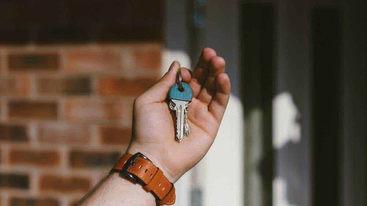 Chiave di casa con guscio blu in una mano, immagine realistica, ambiente domestico, serratura, pronti per entrare o uscire, sicurezza e chiusura della porta.