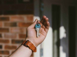 Chiave di casa con guscio blu in una mano, immagine realistica, ambiente domestico, serratura, pronti per entrare o uscire, sicurezza e chiusura della porta.
