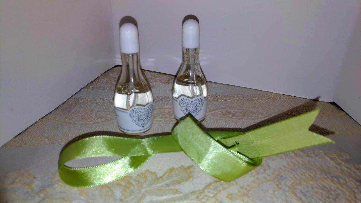 Piccole fiale di profumo con cuore decorato, lunghezza media, in vetro trasparente, sul tavolo di legno con nastro verde brillante e sfondo neutro.