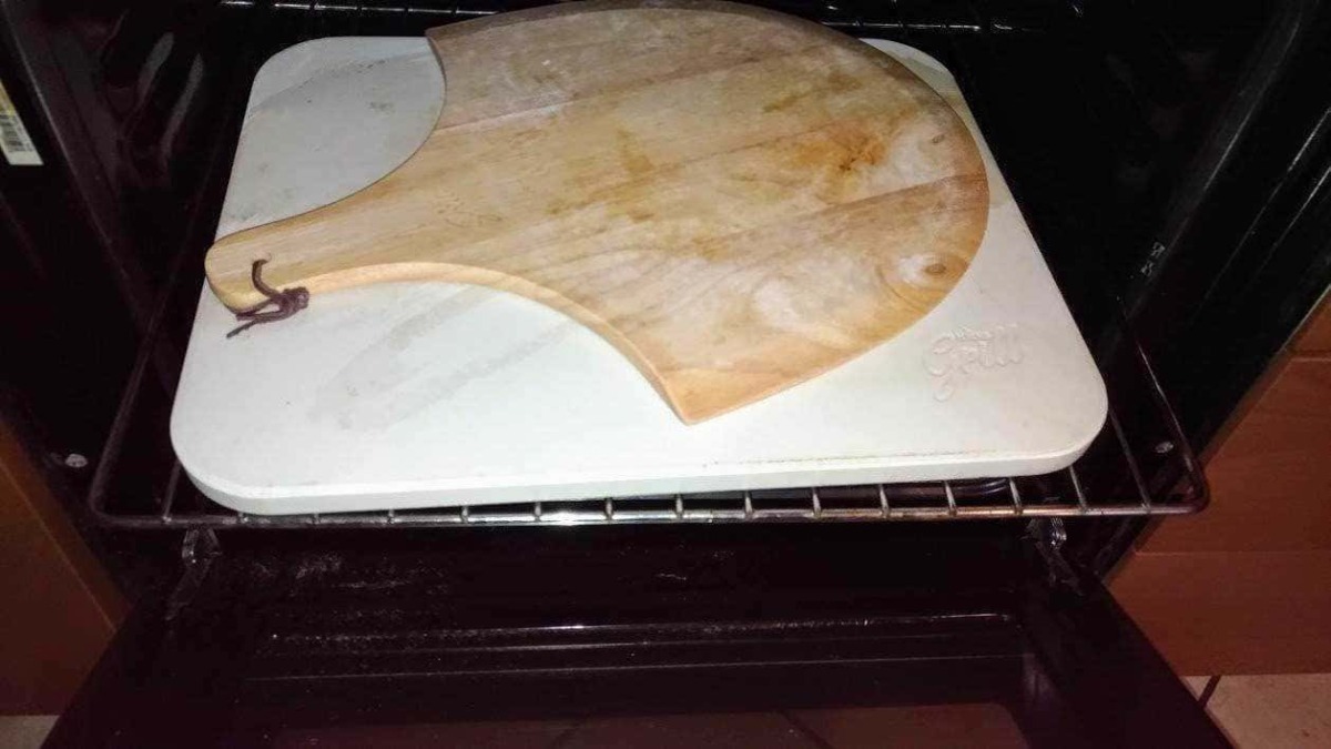 Pietra refrattaria pizzastein: Tagliere in legno su forno con piastra in ceramica, oggetto per preparare cibi, cucina italiana, utensile di cucina tradizionale, attrezzature da cucina rustiche e artigianali.