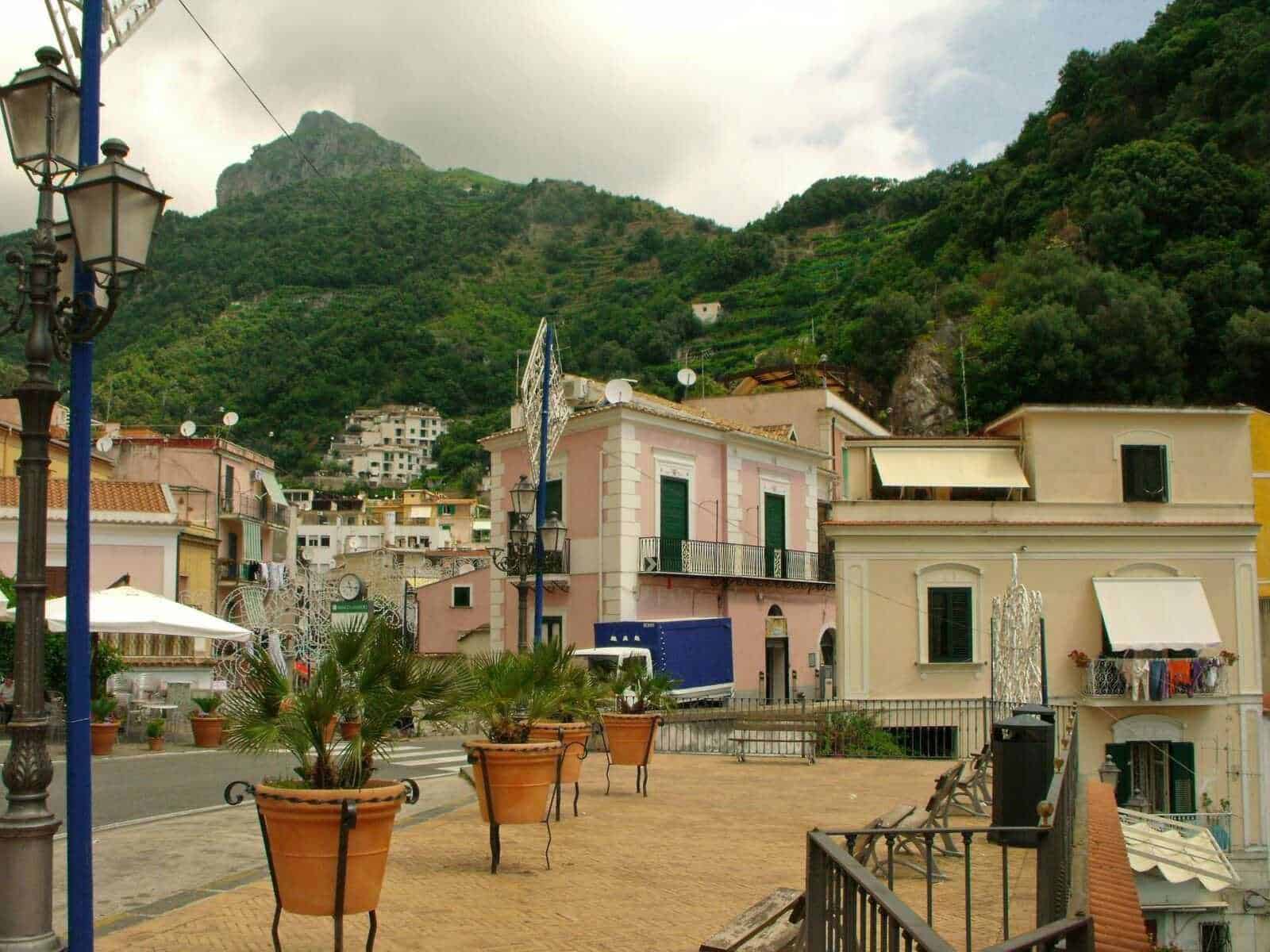 Cetara, paesino sul mare con case colorate e terrazze, situato tra montagne verdi, con panchine e piante in vaso in primo piano, atmosfera tranquilla e suggestiva.