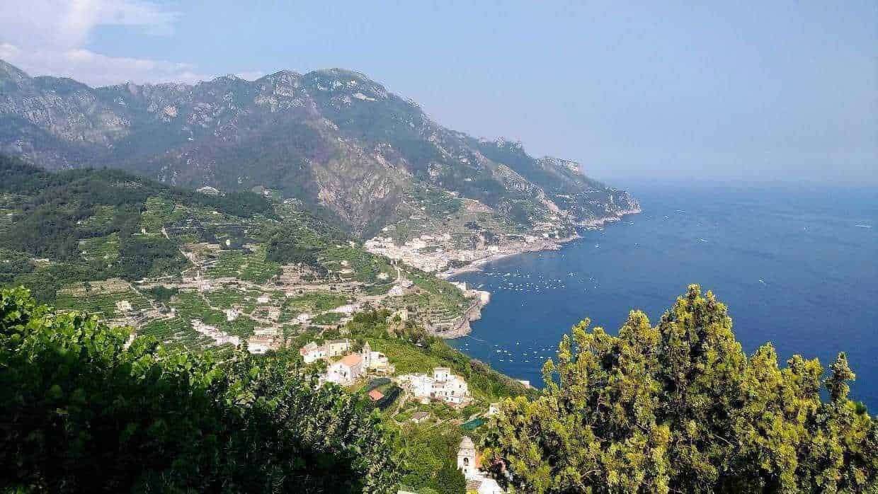 Vista panoramica della Costiera Amalfitana con colline verdeggianti, case bianche e il mare cristallino, ideale per vacanze in Italia.