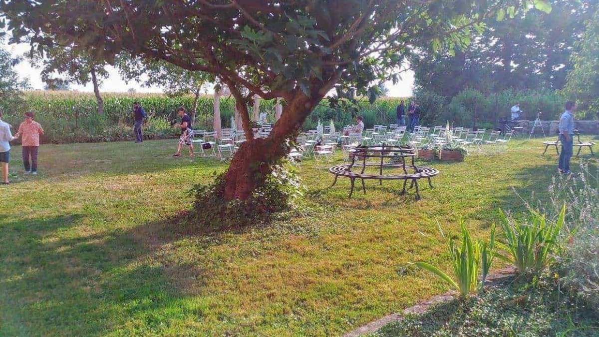 Pranzo all'aperto in giardino con alberi e sedie bianche, atmosfera tranquilla durante il tramonto.
