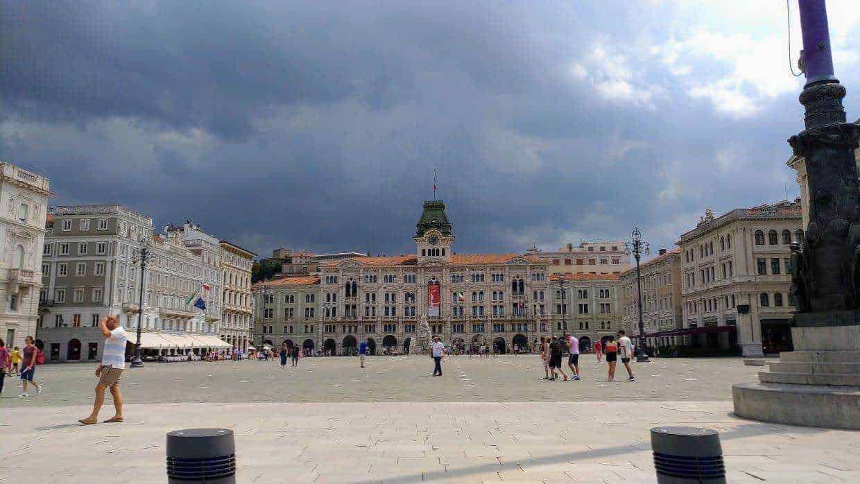 Cappello centrale Piazza Unità d'Italia a Trieste con edifici storici e cielo nuvoloso.