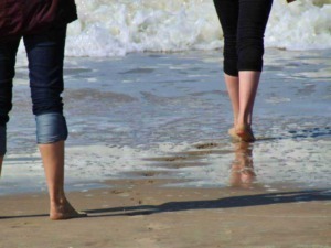 Passeggiata sulla spiaggia con onde che si infrangono, due persone camminano senza scarpe sull sabbia umida, atmosfera rilassante e nature, ideale per vacanze al mare e relax estivo.