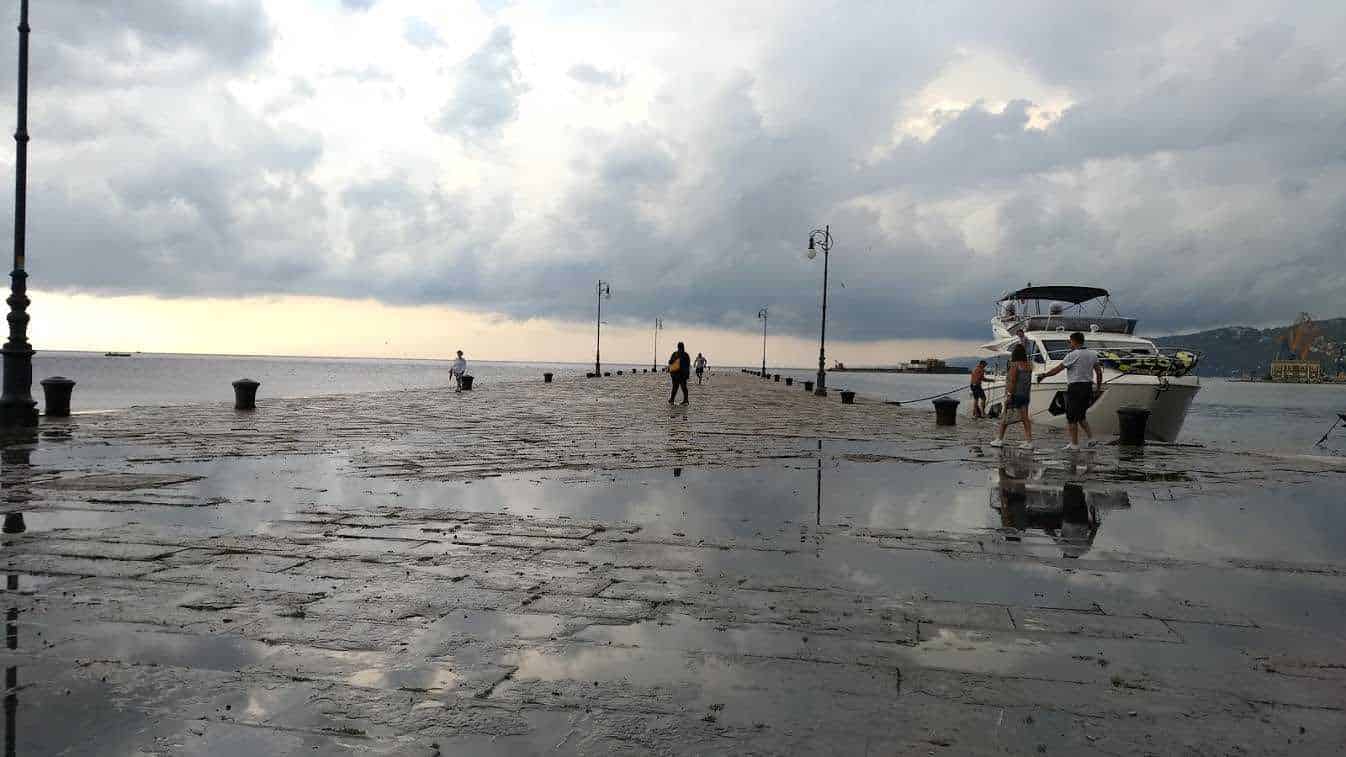 Passerella sul porto di mare con barche e persone che passeggiano, cielo nuvoloso, atmosfera marina e rilassante, ideale per blog di viaggi e destinazioni estive.