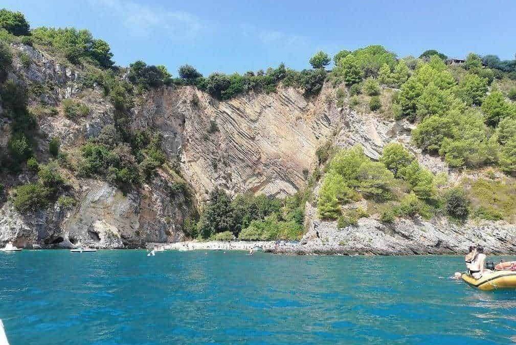 Scogliera e mare blu in Liguria, Italia, con vegetazione verde e barche in acqua, paesaggio naturale e spettacolare destinazione turistica per relax e avventure acquatiche.