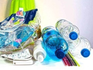Rifiuti di plastica riciclabili con bottiglie di acqua, cannucce e confezioni di plastica su superficie bianca, tema di riciclaggio e tutela ambientale.