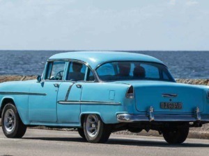 Fiat 500 storica in stile vintage, colore azzurro, parcheggiata vicino al mare con sfondo di cielo e acqua, perfetta per appassionati di auto d’epoca e cultura automobilistica.