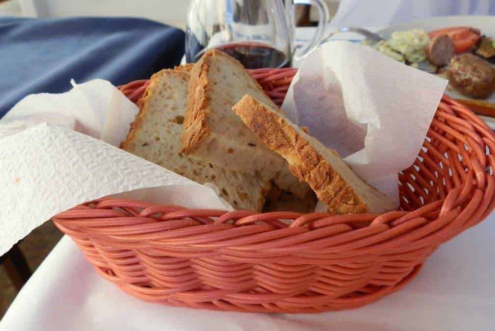 Pane casereccio in cestino con vino rosso e piatto di carne, stile italiano.