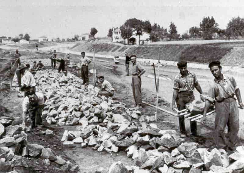 Cantiere di lavoro con operai che posano pietre per la costruzione di una strada, immagine storica di lavori pubblici in Italia.