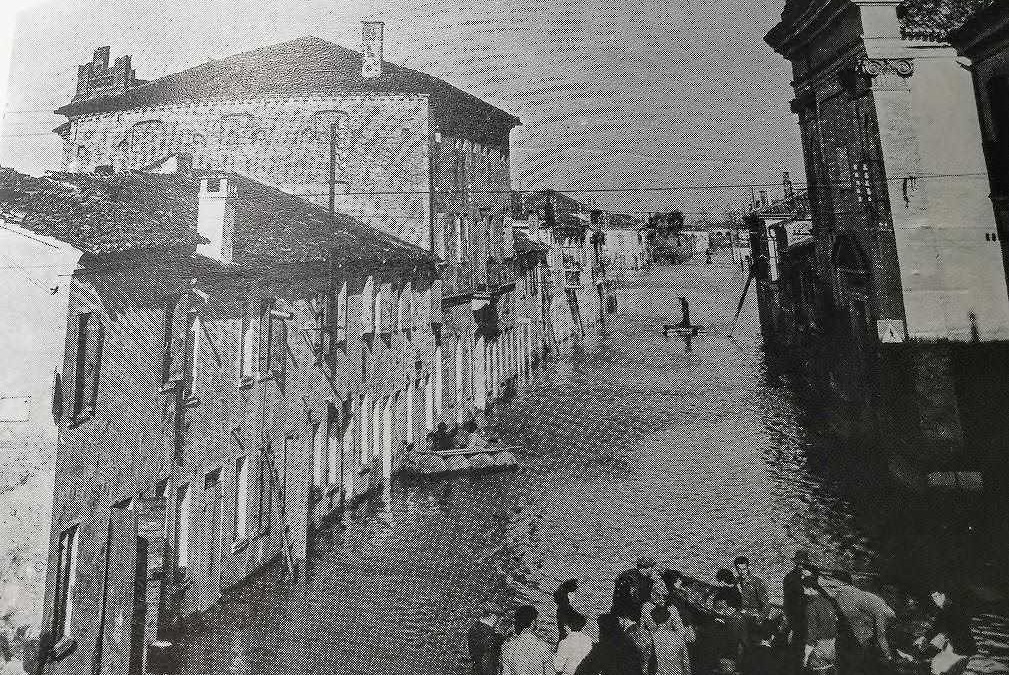 Vecchio scena di un canale veneziano con persone in barca e edifici storici sullo sfondo, in stile vintage e in bianco e nero.