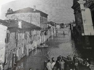 Vecchio scena di un canale veneziano con persone in barca e edifici storici sullo sfondo, in stile vintage e in bianco e nero.
