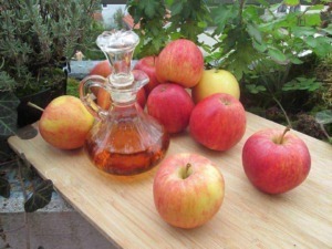 Mele rosse e gialle con bottiglia di sidro di mele artigianale su un tavolo di legno in giardino.