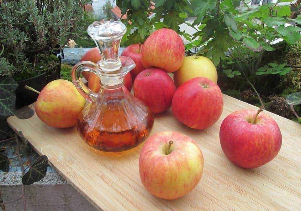 Mele rosse e gialle con bottiglia di sidro di mele artigianale su un tavolo di legno in giardino.