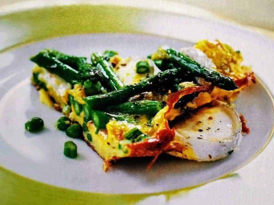 Uova strapazzate con asparagi e piselli, servite in un piatto bianco elegante, ideale per colazioni e brunch salutari. Ricetta semplice e ricca di verdure fresche e proteine.