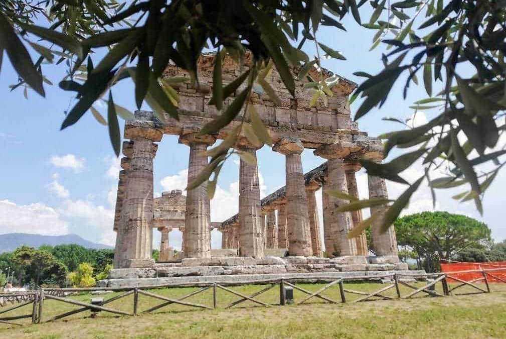 Antico tempio greco antico con colonne di pietra, situato in un sito archeologico all'aperto, circondato da vegetazione e cielo azzurro, rappresenta un importante sito storico e culturale.