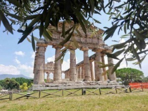 Antico tempio greco antico con colonne di pietra, situato in un sito archeologico all'aperto, circondato da vegetazione e cielo azzurro, rappresenta un importante sito storico e culturale.