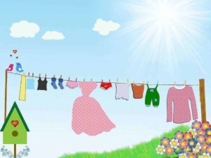 Vestiti stesi ad asciugare al sole in un cortile con prato verde e fiori colorati, scenario di una giornata di primavera o estate, con nuvole e cielo azzurro.