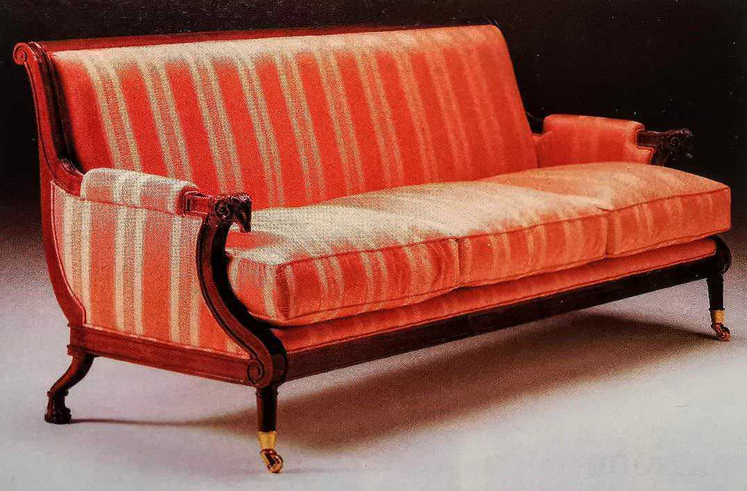 Antico divano in velluto rosso con dettagli in legno intagliato e ruote, stile classico ed elegante, perfetto per arredare un soggiorno di charme o un ambiente vintage.