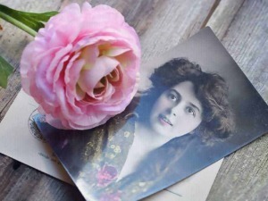 Farfalla rosa posata su una fotografia vintage di una donna con capelli ricci, su un tavolo di legno rustico.