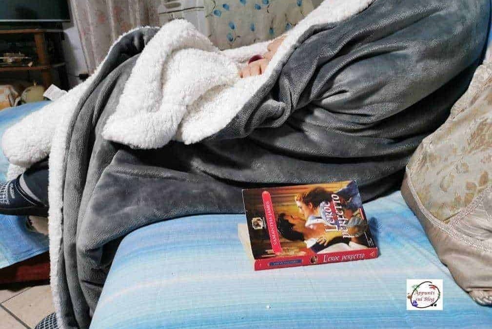 Sognatore sdraiato su un divano con coperta grigia e libro aperto, ambiente casalingo confortevole, atmosfera rilassante, ideale per leggere o riposare.