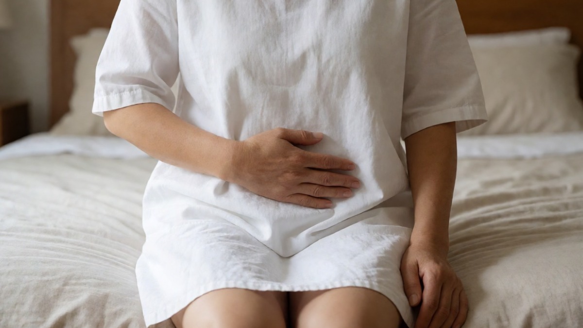Dolore addominale e ginecologico, donna seduta su letto con mano sulla pancia, problema di salute femminile, disfunzione o malattia ginecologica, immagine medica per blog di salute e medicina.