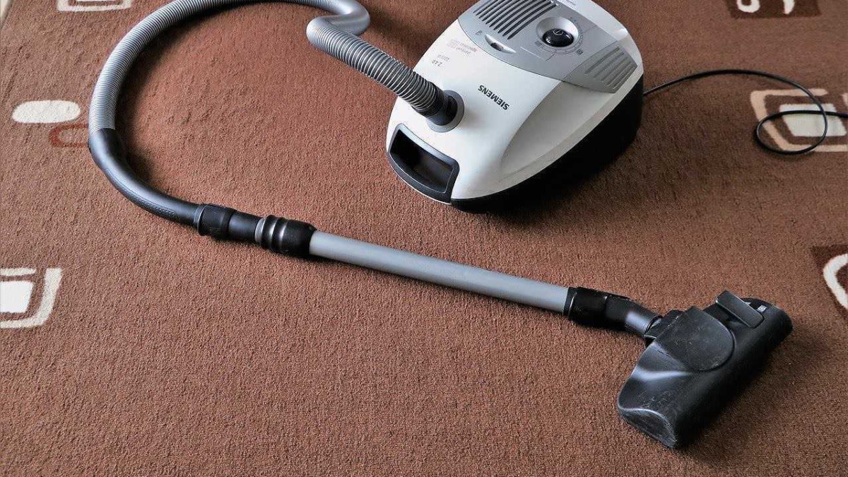 Aspirapolvere Siemens con tubo flessibile e bocchetta per pulizia di pavimenti e tappeti sul tappeto color marrone con motivi geometrici.