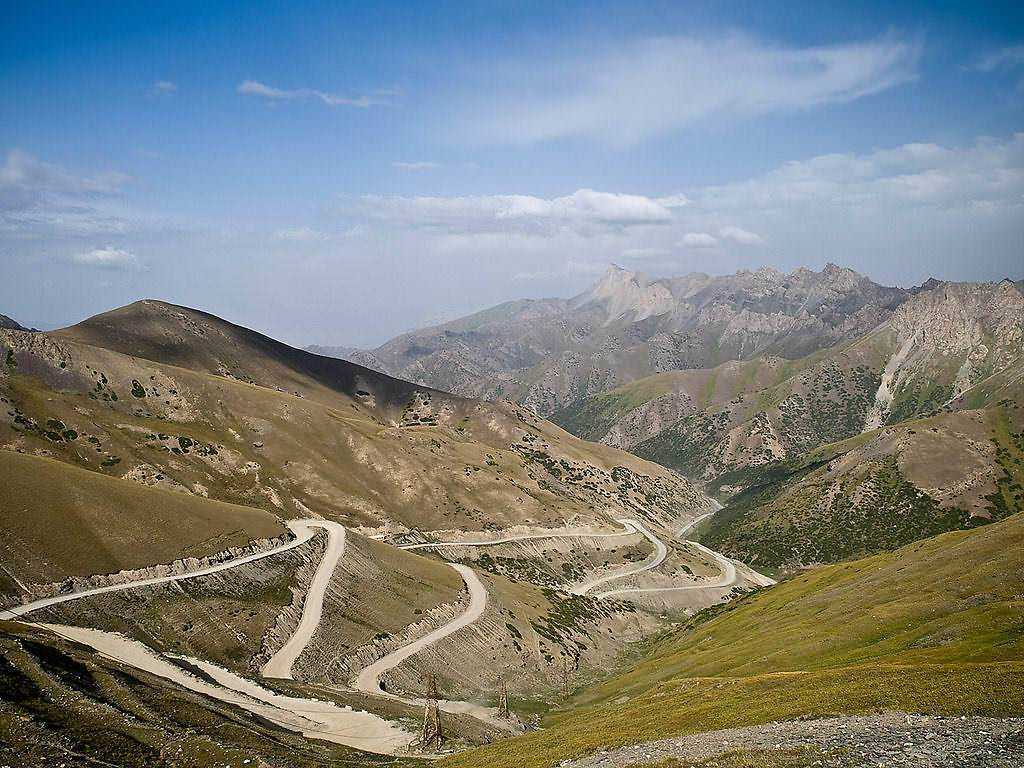 Strada di montagna con curve strette tra colline e montagne, paesaggio naturale, cielo nuvoloso, vista panoramica, escursioni in natura, viaggio e avventura.