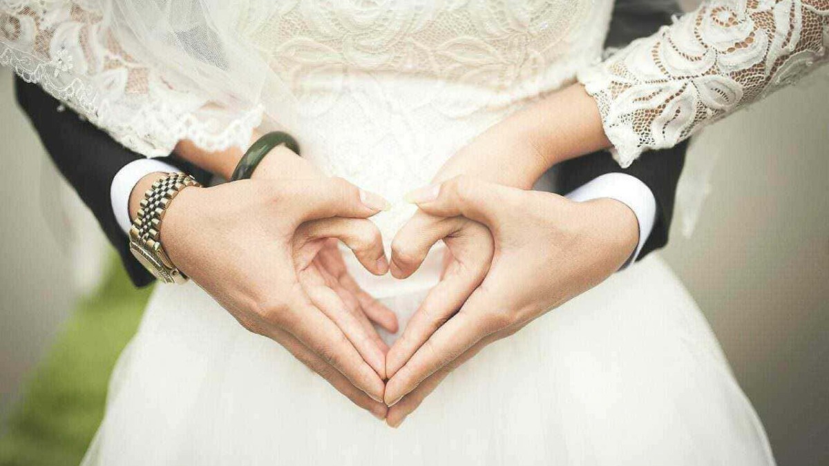 Cuori fatti con le mani di una coppia di sposi in abiti da matrimonio durante la cerimonia nuziale.