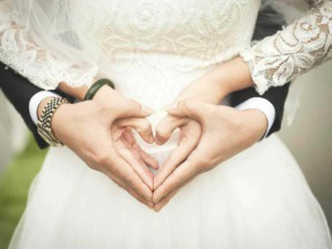 Cuori fatti con le mani di una coppia di sposi in abiti da matrimonio durante la cerimonia nuziale.