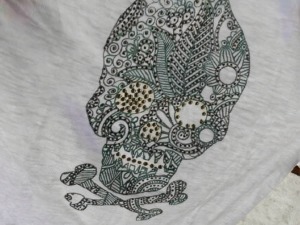 Disegno di teschio stilizzato con dettagli intricati e pattern artistici su tessuto bianco, ideale per decorazioni e arte moderna. Perfetto per chi apprezza l'arte urbana e design originali.