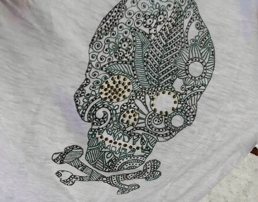 Disegno di teschio stilizzato con dettagli intricati e pattern artistici su tessuto bianco, ideale per decorazioni e arte moderna. Perfetto per chi apprezza l'arte urbana e design originali.