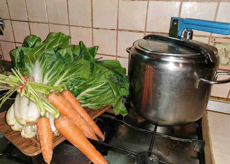 Carote e cicoria fresche su ripiano vicino a pentola sul fornello in cucina.