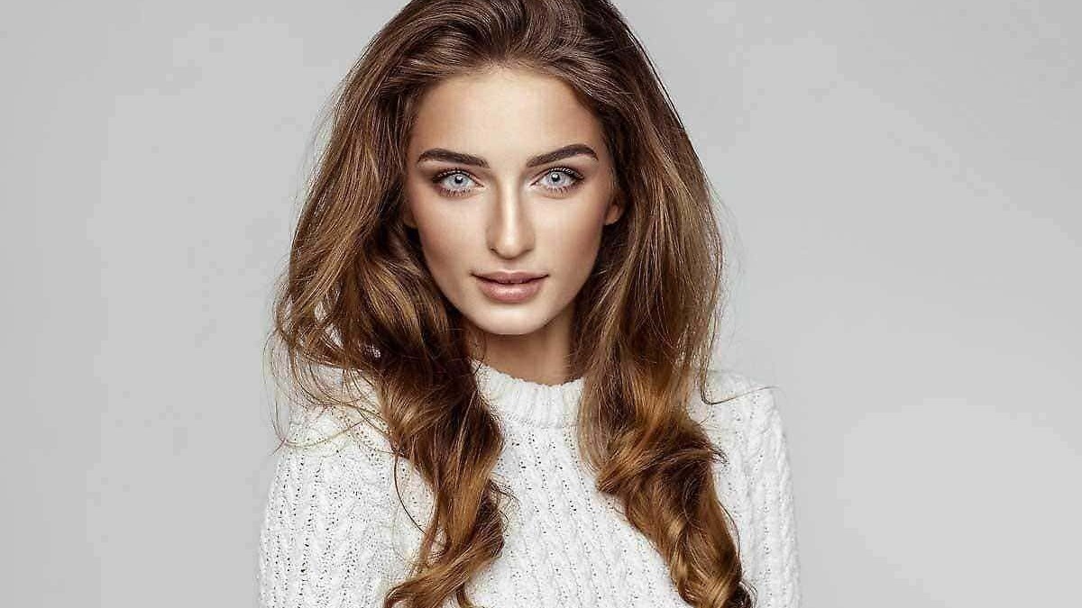 Capelli lunghi e mossi, bellezza naturale e trucco leggero, modello femminile in abbigliamento casual, sfondo grigio chiaro, stile moda e bellezza.