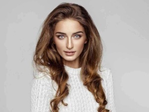 Capelli lunghi e mossi, bellezza naturale e trucco leggero, modello femminile in abbigliamento casual, sfondo grigio chiaro, stile moda e bellezza.