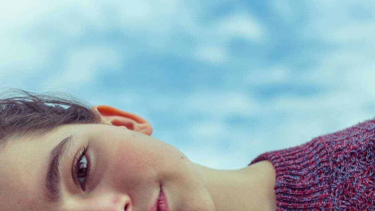 Cielo sereno e tranquillo con primo piano di donna con occhi penetranti e capelli corti, indossa maglione viola, immagine rilassante e di stile contemplativo.