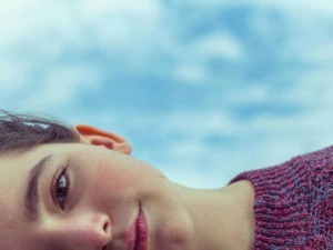 Cielo sereno e tranquillo con primo piano di donna con occhi penetranti e capelli corti, indossa maglione viola, immagine rilassante e di stile contemplativo.