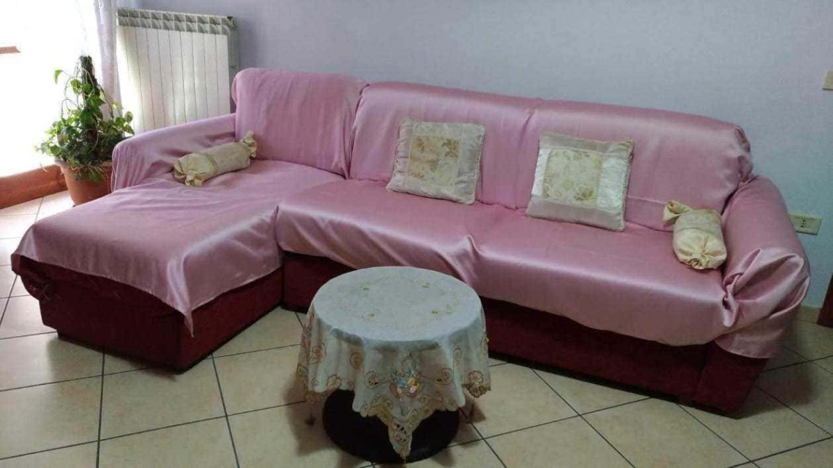 Confortevole divano rosa con cuscini decorativi e copridivano, arredamento da soggiorno elegante e accogliente, ideale per ambienti domestici arredati in stile classico.