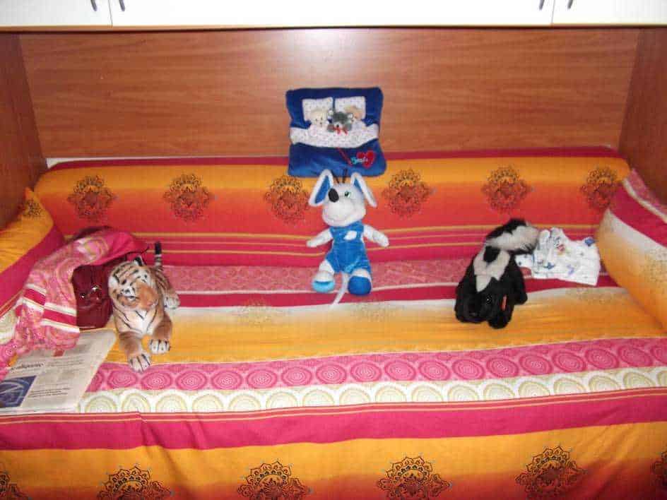 Gattino di peluche e bambole posizionate sul letto con copriletto arancione e rosa, arredamento di camera da letto, decorazioni e oggetti morbidi.