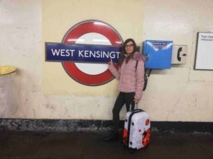 West Kensington stazione della metropolitana di Londra con viaggiatrice che tiene la valigia davanti al simbolo della metropolitana.