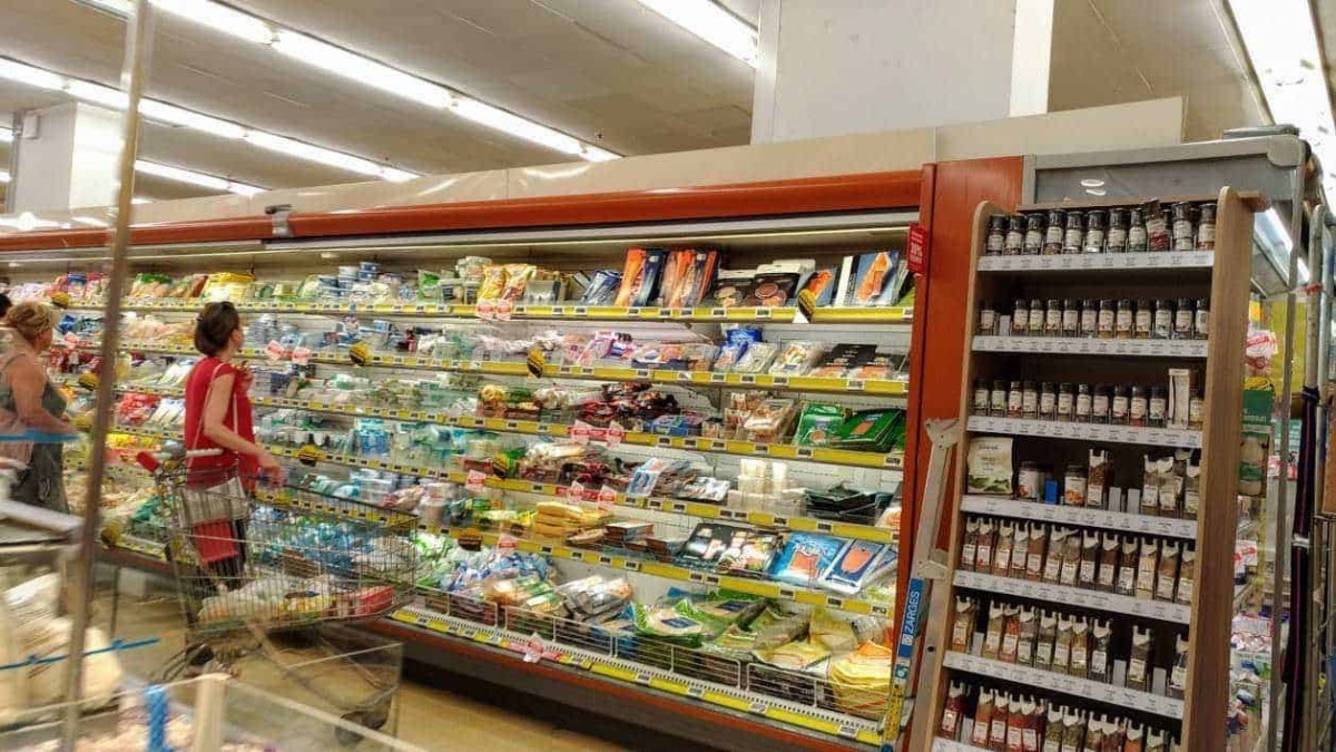 Bambini e adulti fanno acquisti in un supermercato all'aperto, con vasta gamma di prodotti alimentari e spezie. Un'ambientazione di supermercato con scaffali pieni di generi alimentari in esposizione.