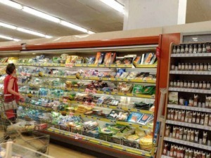 Bambini e adulti fanno acquisti in un supermercato all'aperto, con vasta gamma di prodotti alimentari e spezie. Un'ambientazione di supermercato con scaffali pieni di generi alimentari in esposizione.