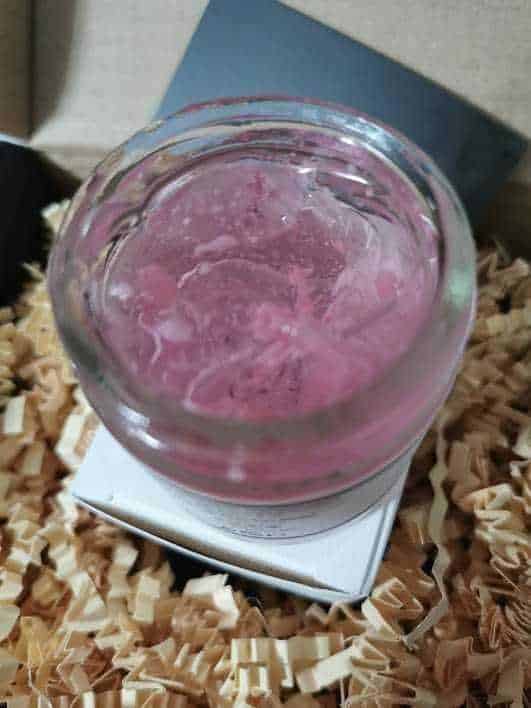 Vasetto di vetro con pasta di rose rosa chiaro su supporto bianco, decorato con legno di frassino, ideale per cosmetici fatti in casa o regali naturali.