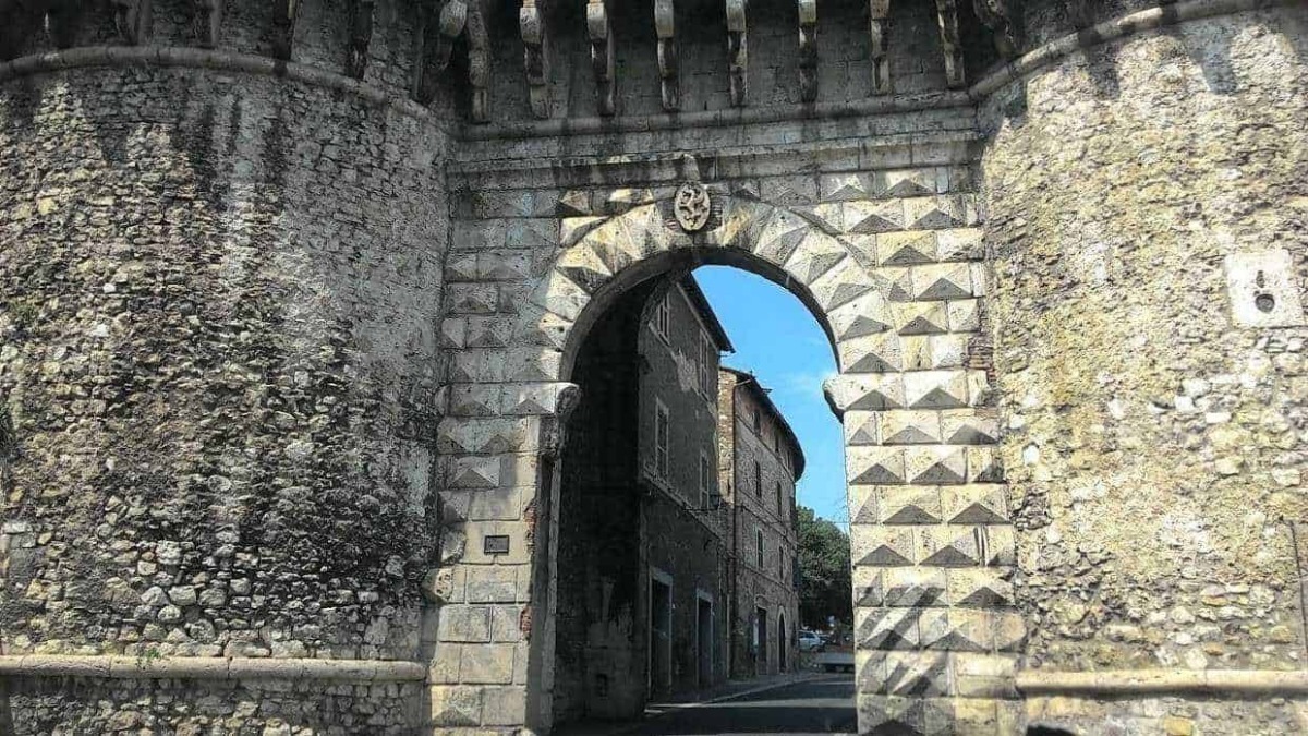 Antica porta in pietra e mattoni, ingresso storico in un pittoresco borgo italiano, con edifici tradizionali e cielo azzurro sullo sfondo.